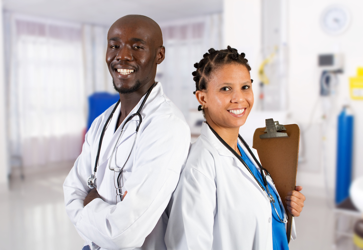 Two medical professionals standing back to back and smiling towards the camera
