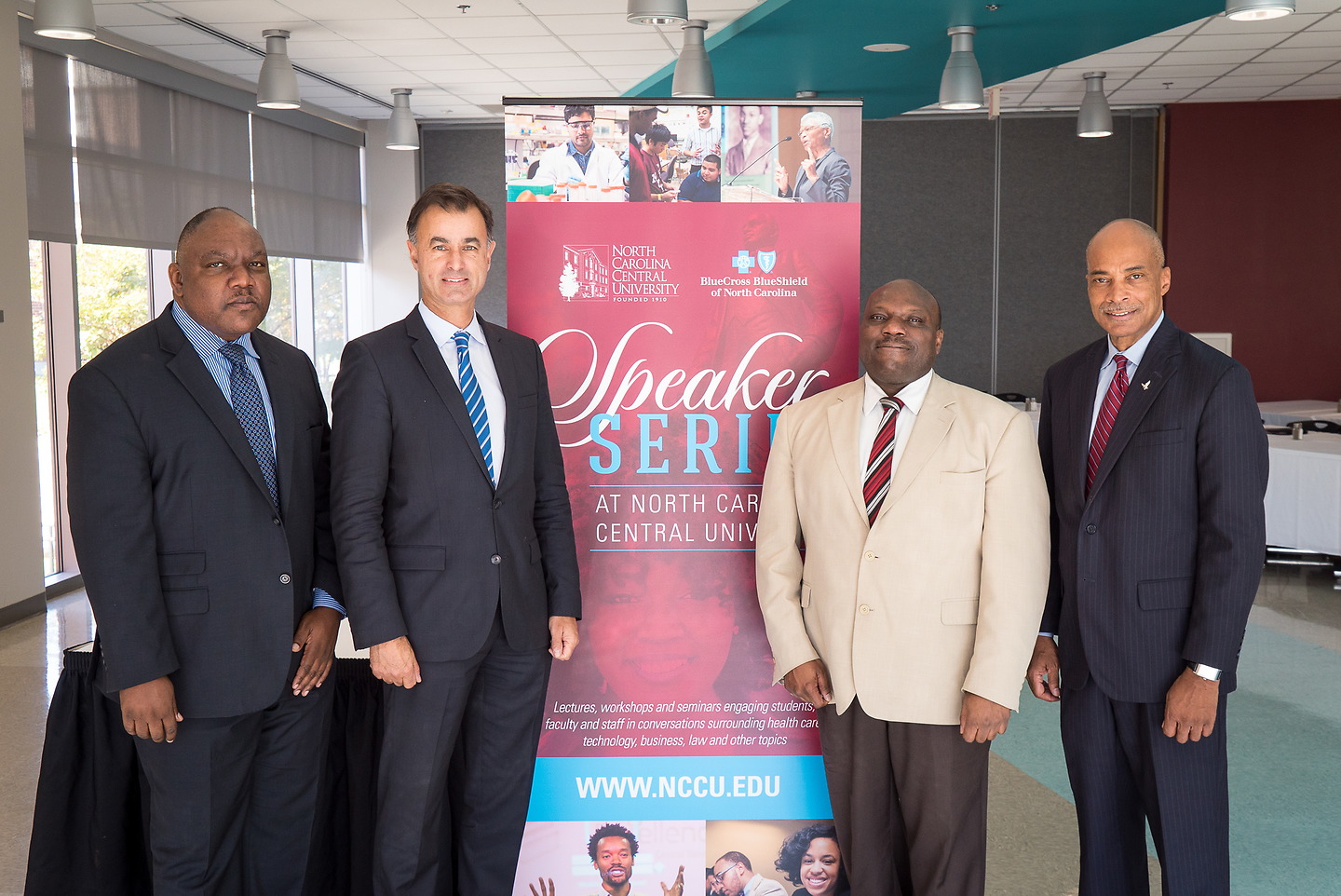 4 people standing in front of a sign smiling at the camera.