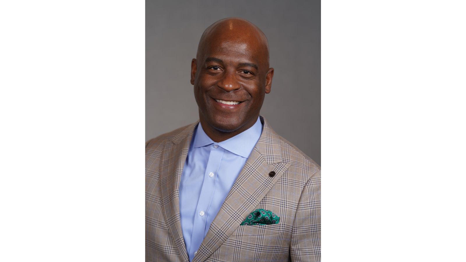 Professional headshot of Rob Robertson wearing a light plaid suit jacket, light blue dress shirt, and patterned pocket square, smiling against a gray background.