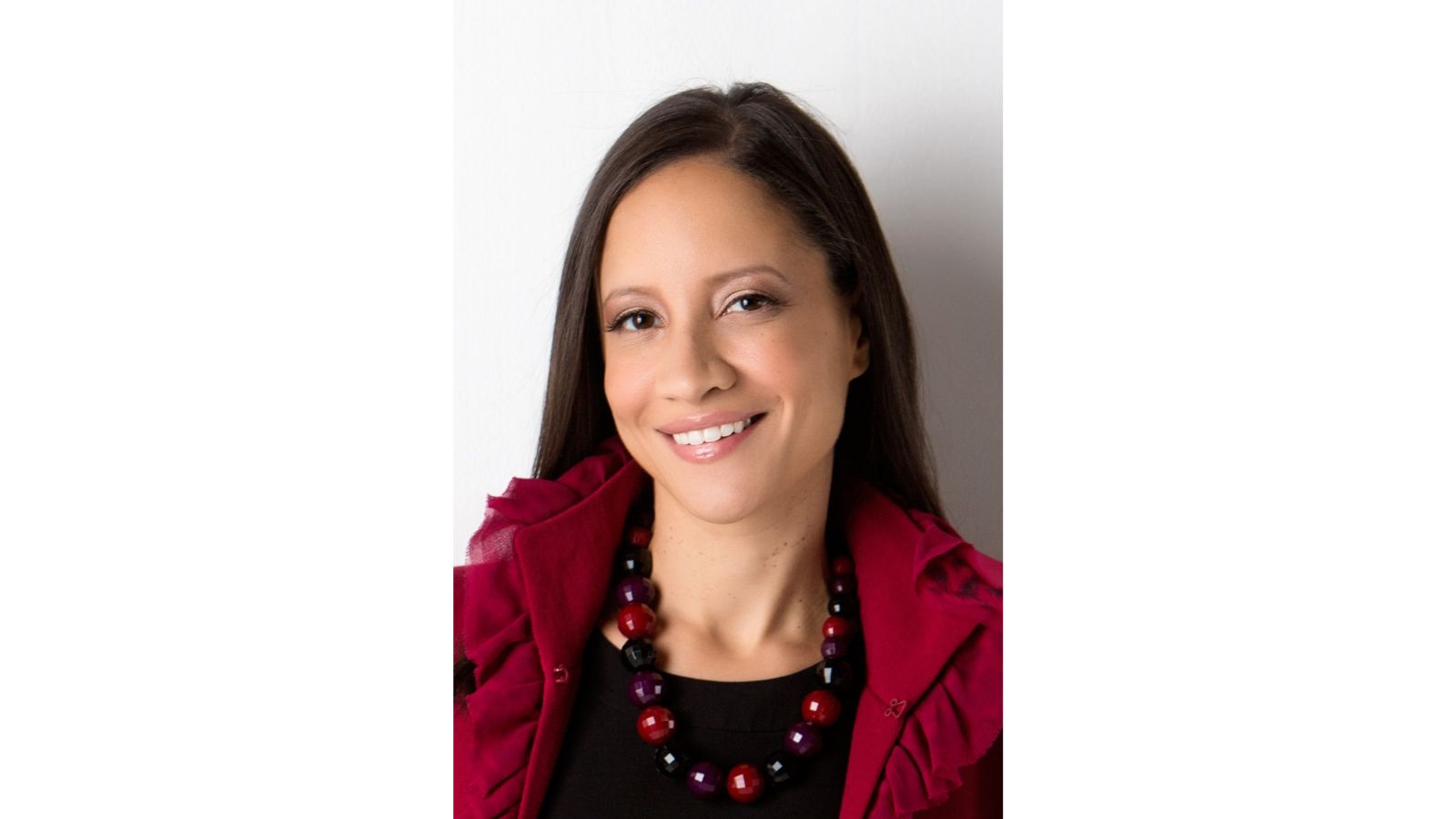 Professional headshot of Anne Sempowski Ward wearing a red jacket with ruffled trim and a black and red beaded necklace, posed against a plain white background.
