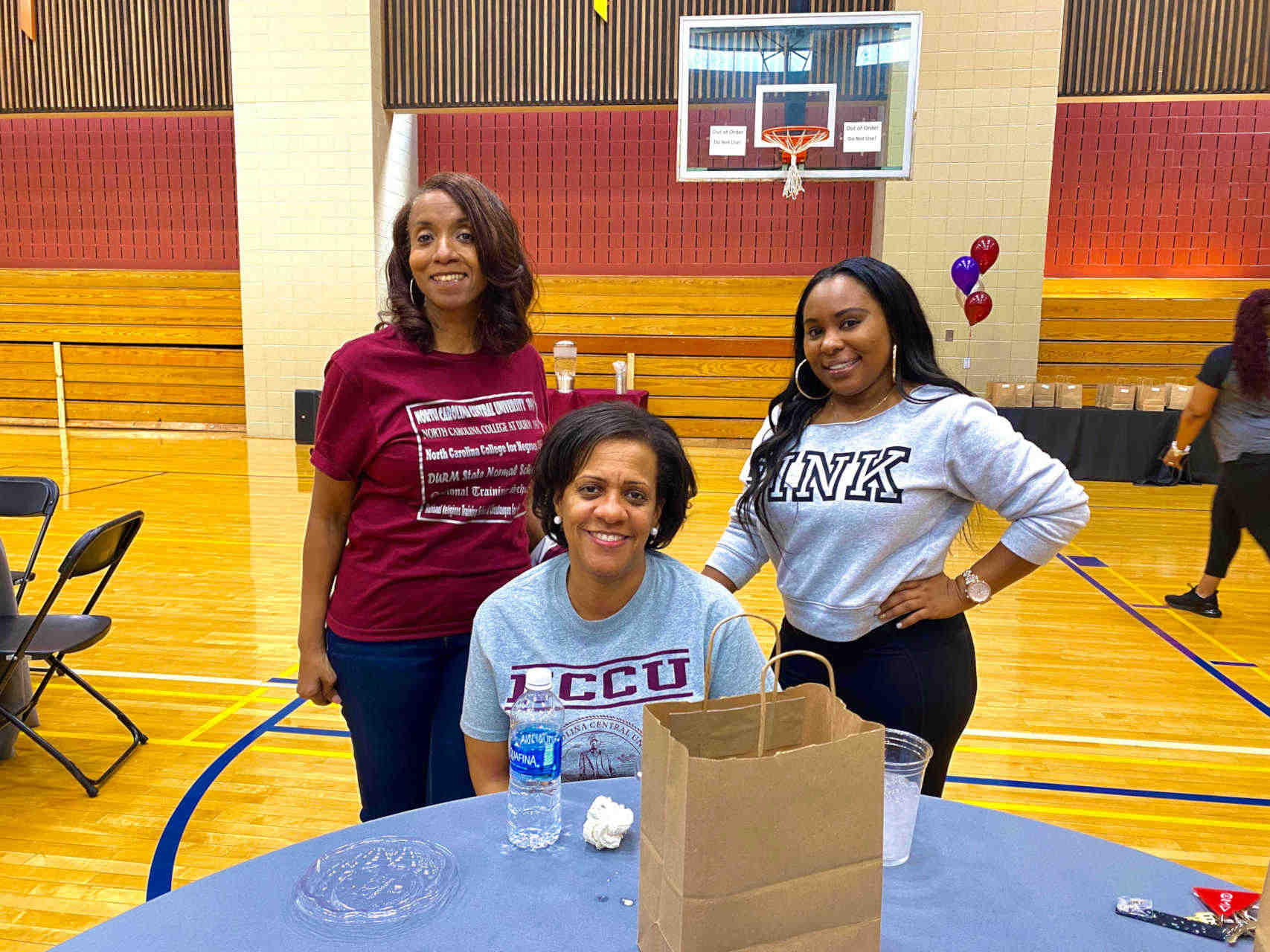 Three women smiling for the camera in the NCCU gymnasium