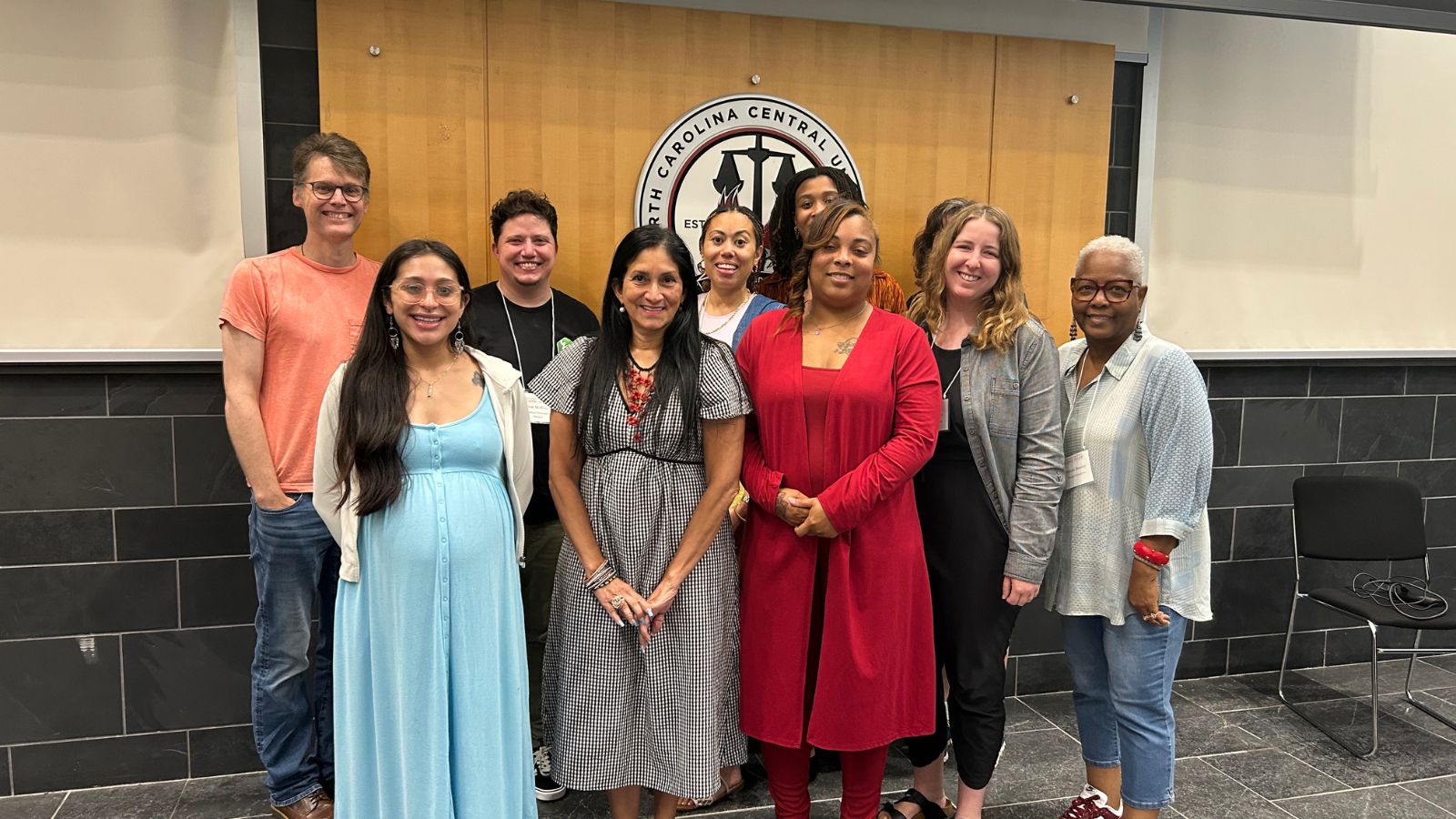 Group photo of nine North Carolina Central University faculty and staff members standing together in front of an NCCU logo backdrop, smiling after a campus meeting or workshop.