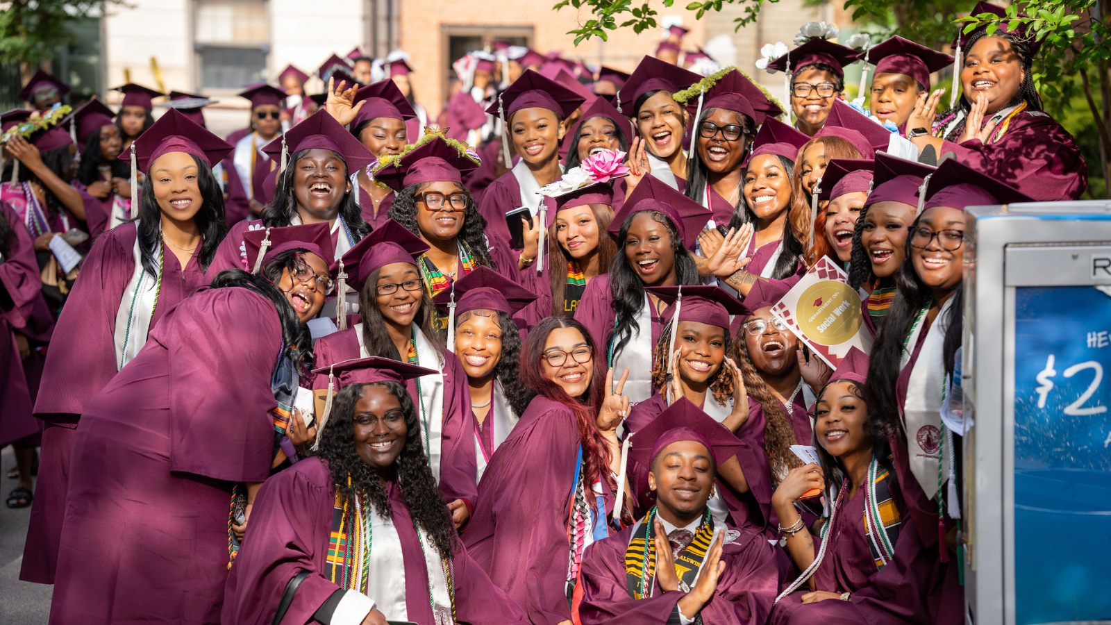 Group of North Carolina Central University graduates in maroon caps and gowns celebrating outdoors during commencement with smiles, honor cords, and decorated graduation caps.