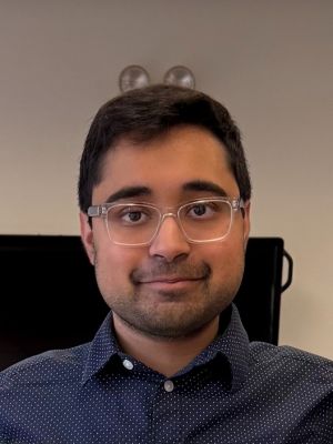 Professional headshot of Asaad wearing glasses and a navy blue button-down shirt.
