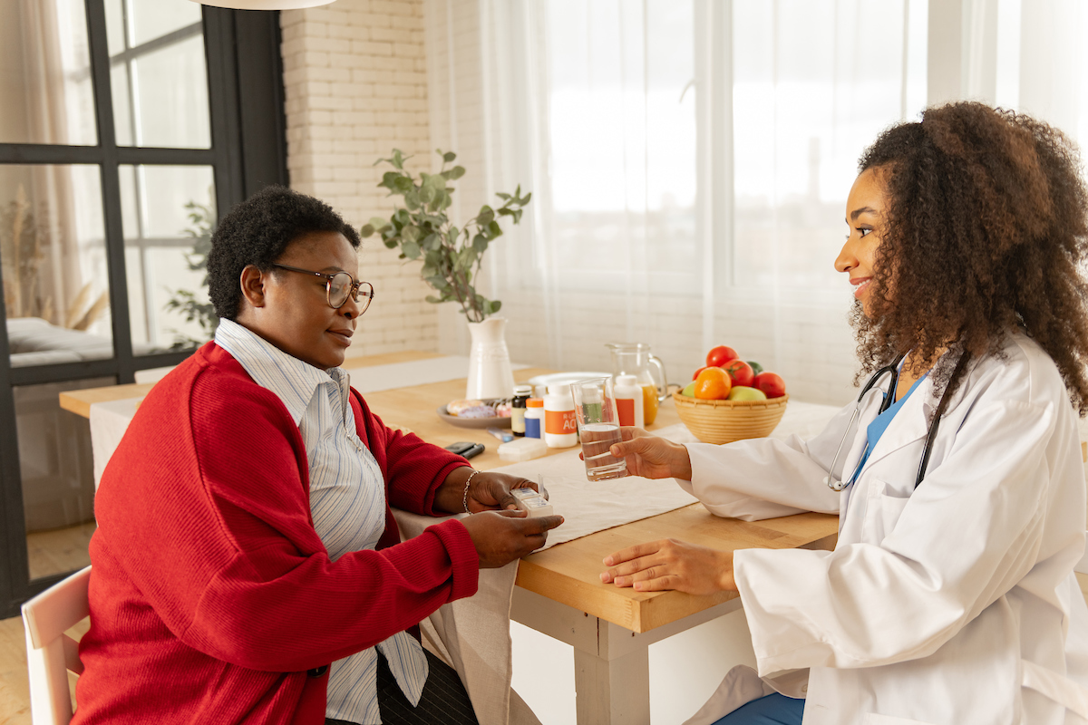 Caring Nurse Giving Pills And Glass Of Water To Aged Woman