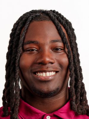 Carl Dean II headshot portrait, smiling professional wearing a maroon collared shirt against a white background.