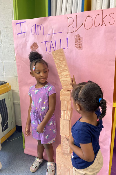 Child measuring another child with building blocks