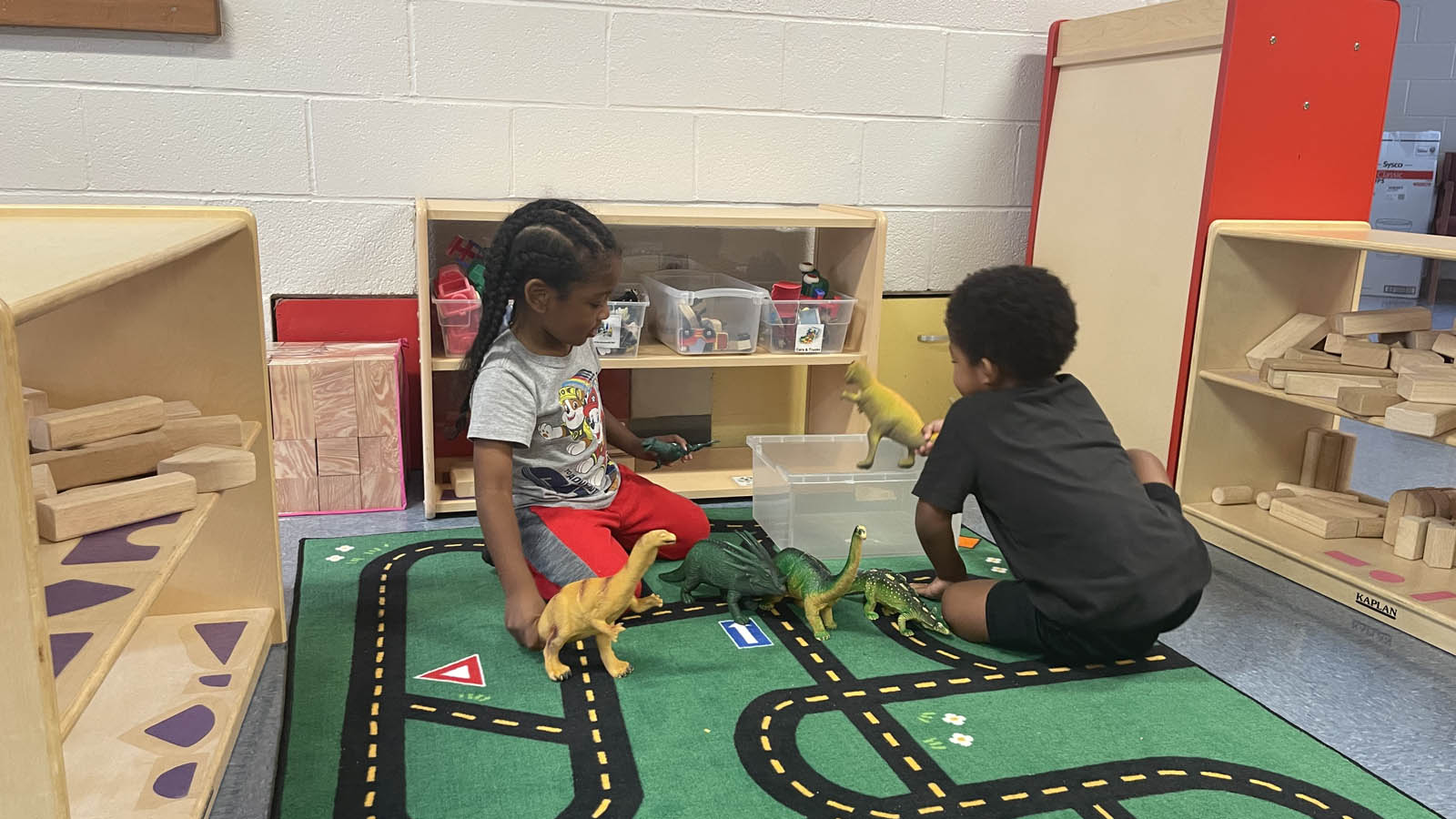 children, sitting on a rug, playing with toy dinosaurs 