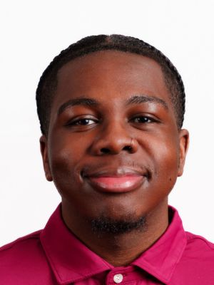 Derek McCoy headshot portrait, smiling professional wearing a maroon collared shirt against a white background.