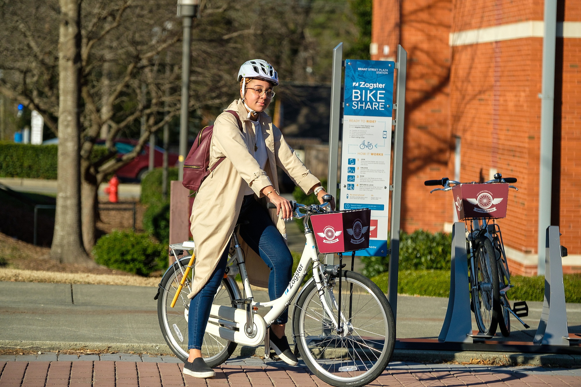 Student is sitting on Bike in-front of Zagster Bike share poster