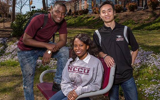 One student sitting in a chair with two standing