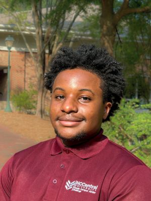 Portrait of Micah wearing a maroon North Carolina Central University polo shirt outdoors.