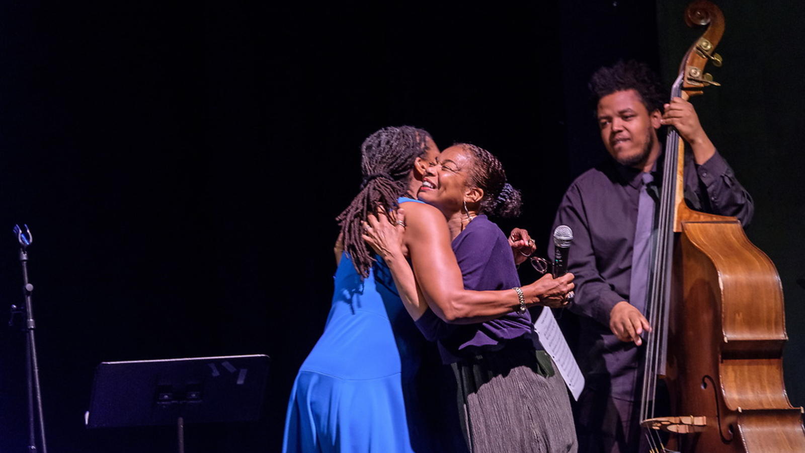 Two women hugging on stage with bassist in background