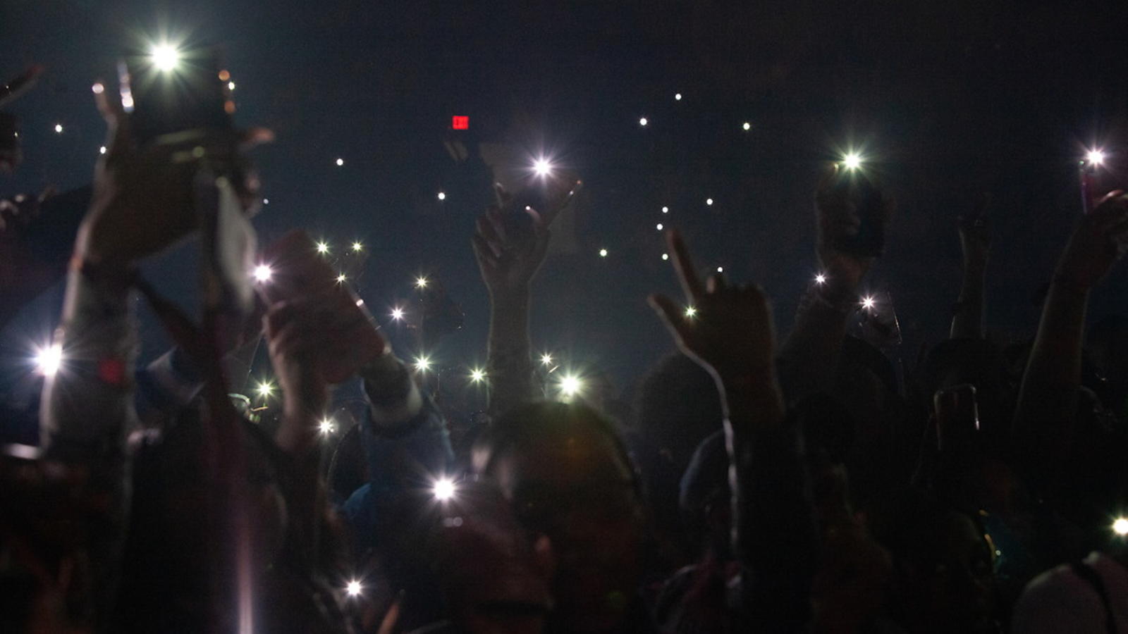 Picture of a dark room with lots of students flashing cellphone lights at the stage.