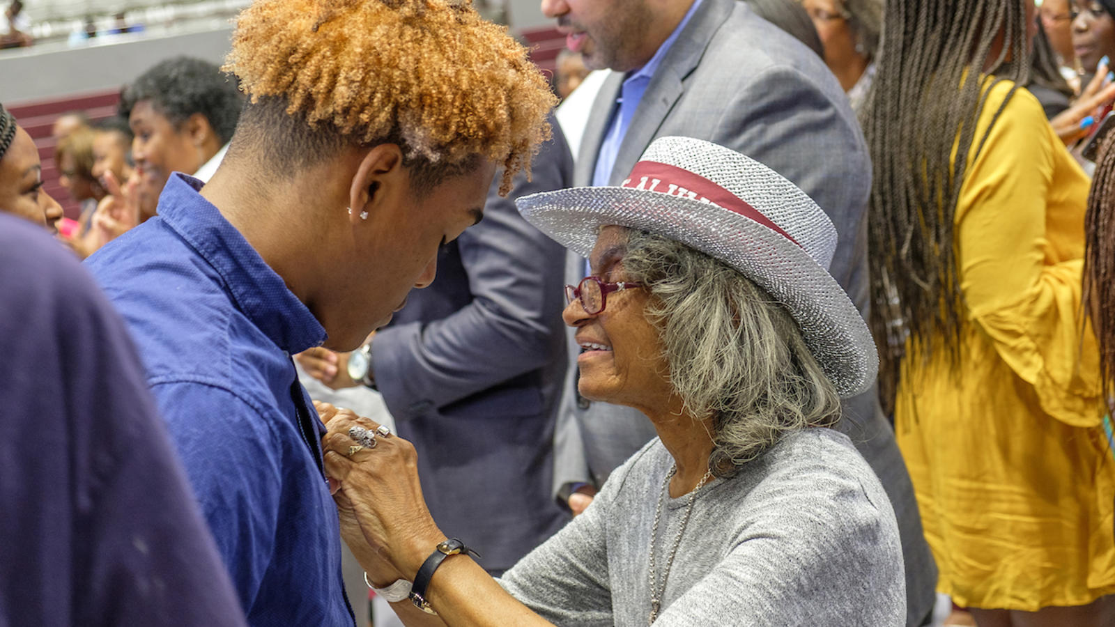 Young man being pinned by an elder in an auditorium 