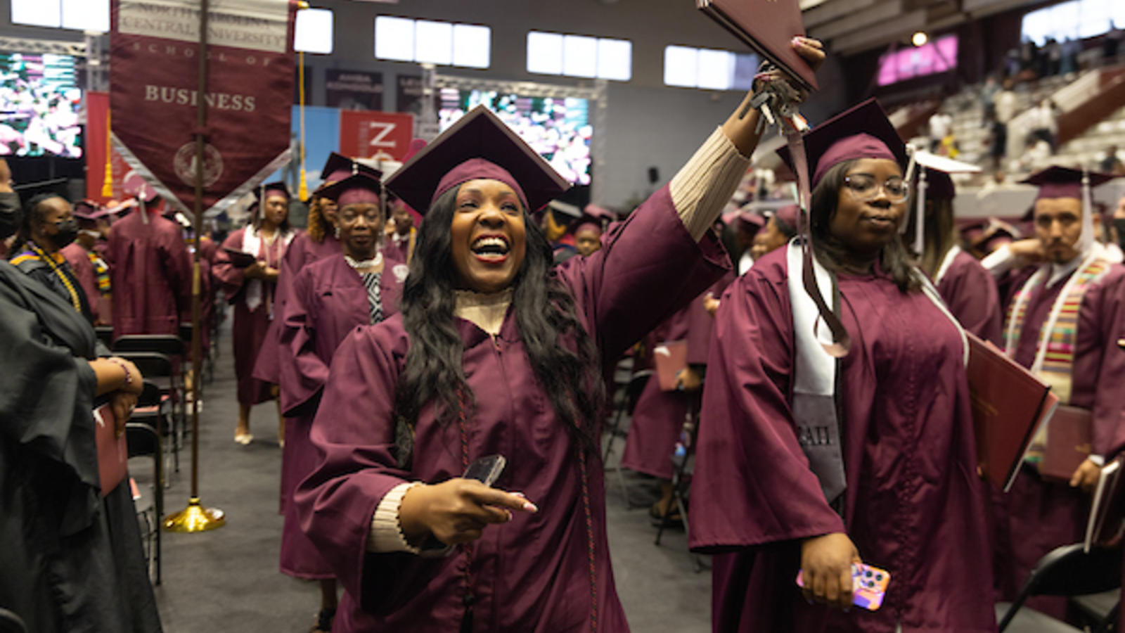 Procession of NCCU graduates at commencement. Woman in foreground is smiling.