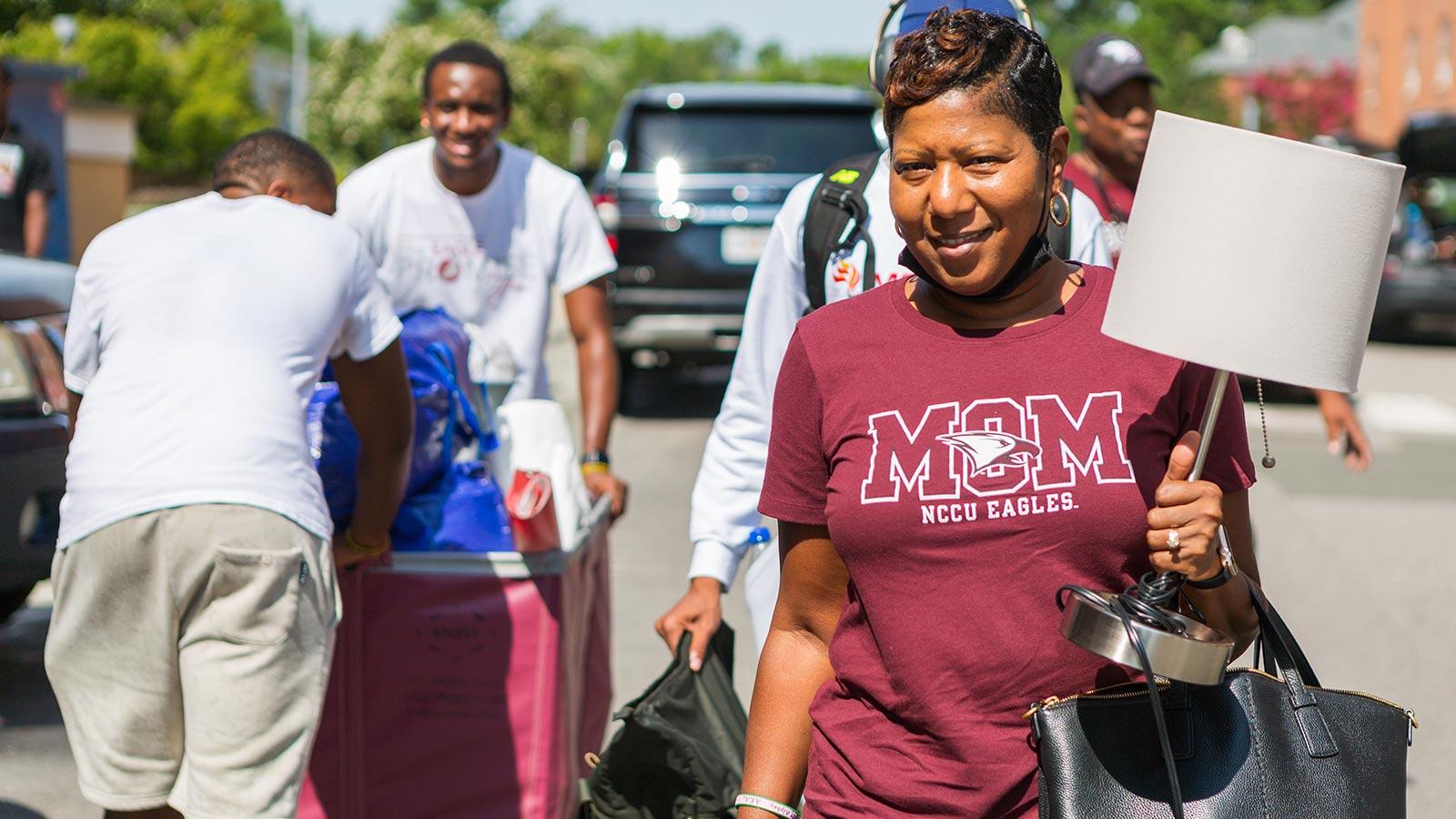 nccu mom holding a lamp with people from nccu community in the background