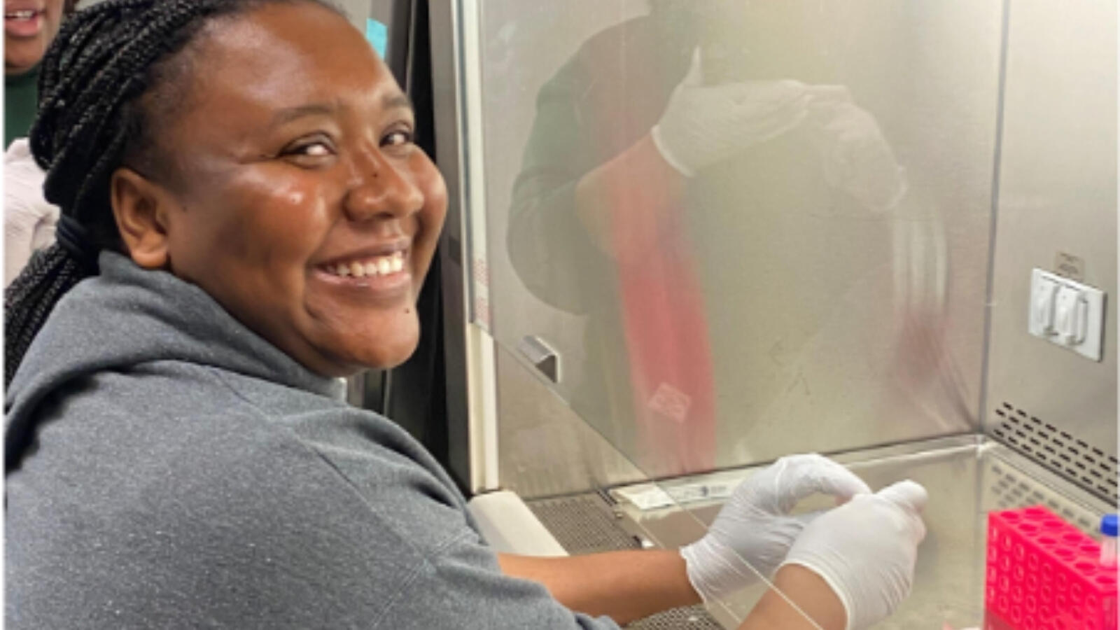 Student working in laboratory hood wearing gloves and smiling while handling samples.