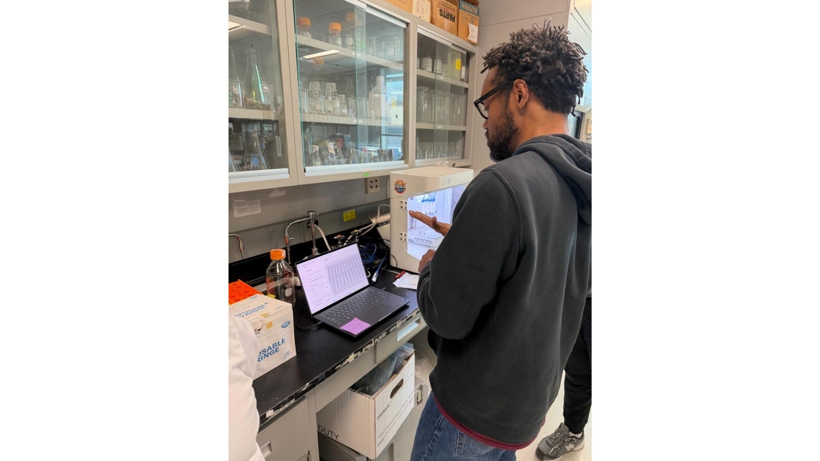 Researcher using laptop to monitor lab equipment and experimental data in science lab.