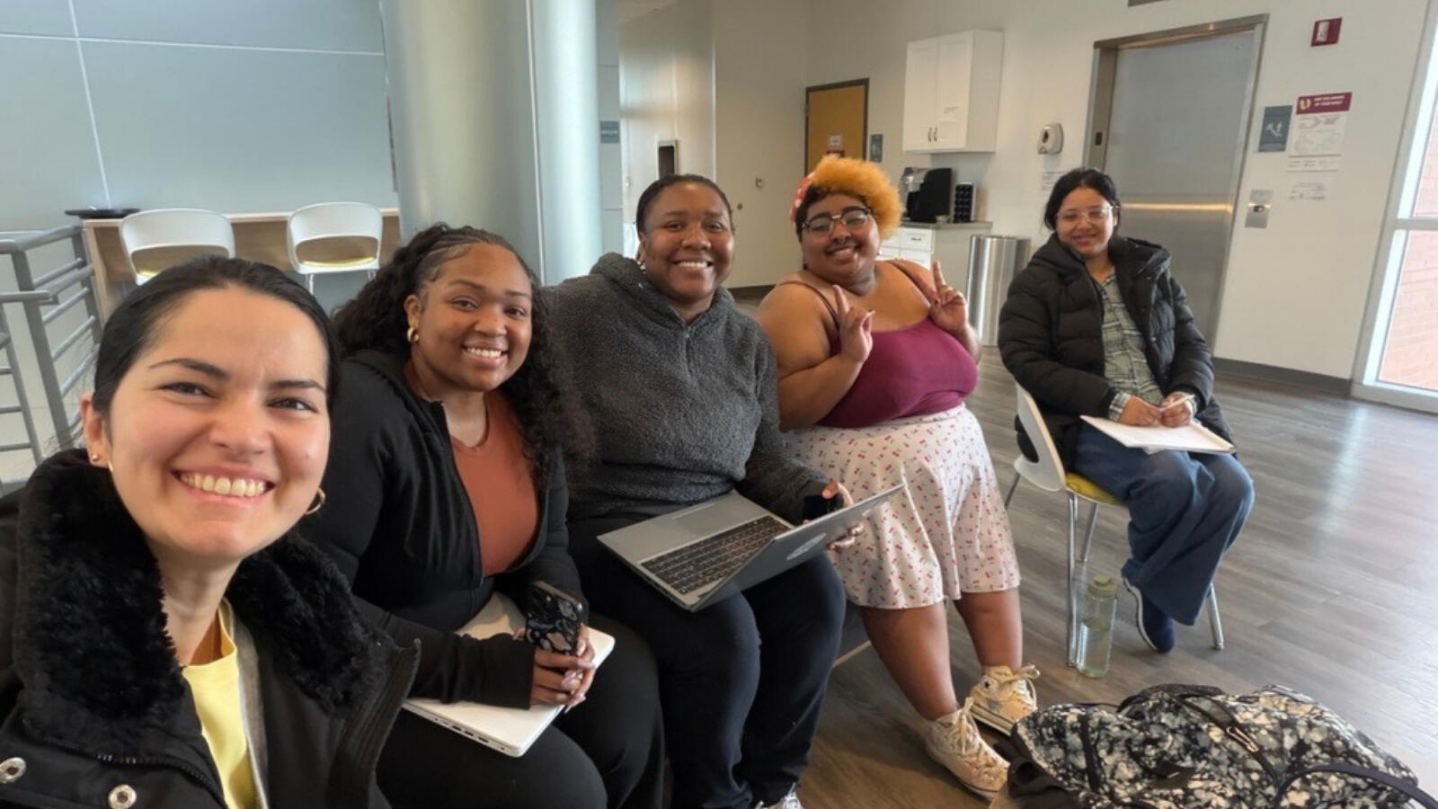 Diverse group of students sitting together with laptops and notebooks in learning space.