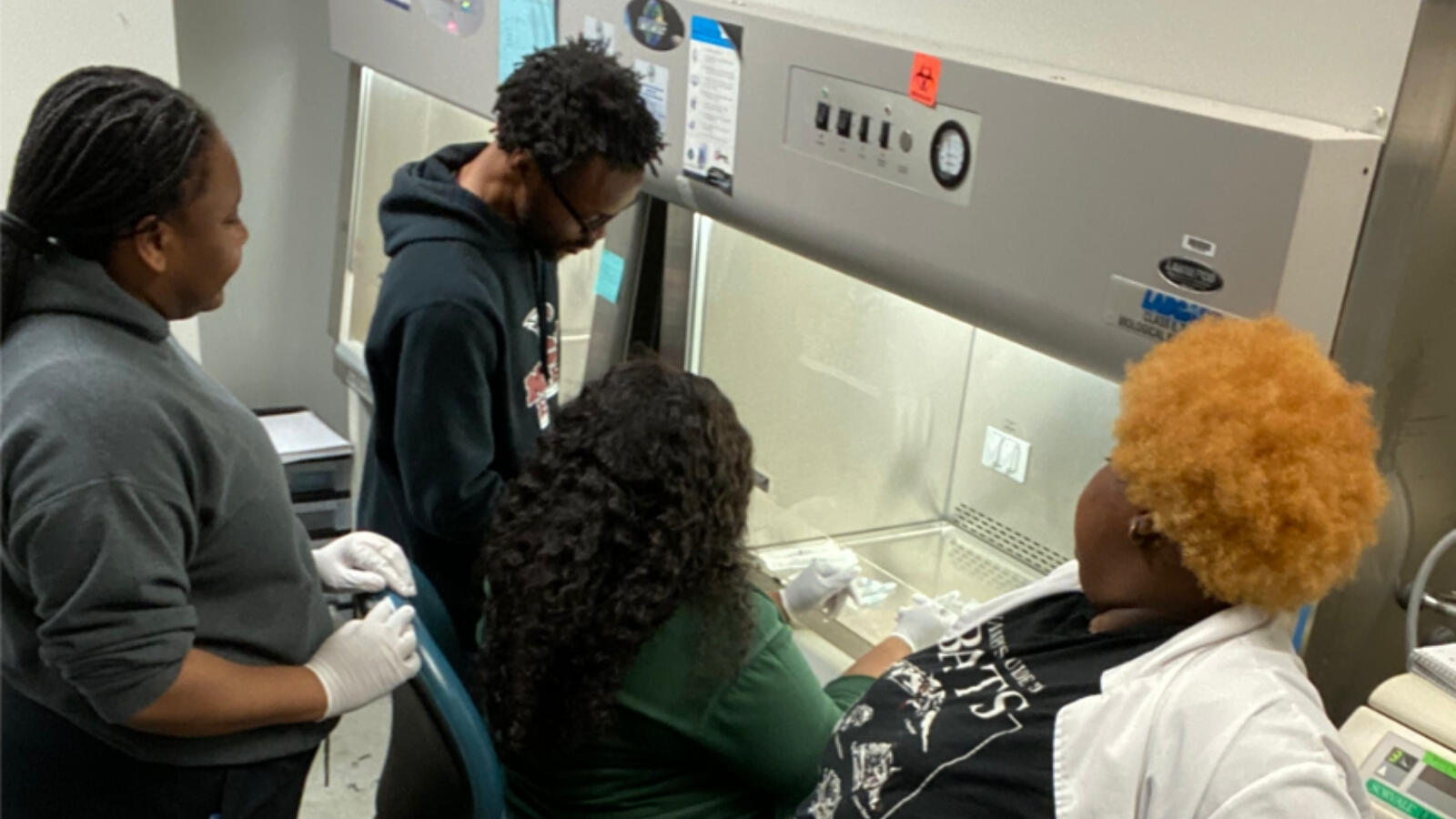 Students working together in lab environment using biosafety cabinet and lab equipment.