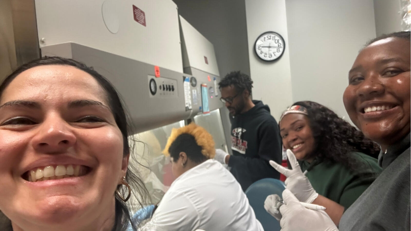 Lab students wearing gloves conducting experiment and posing for photo in research lab.