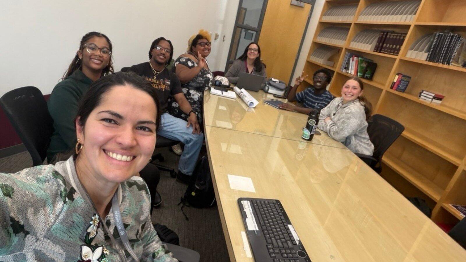 Group of students gathered around conference table collaborating in classroom setting.