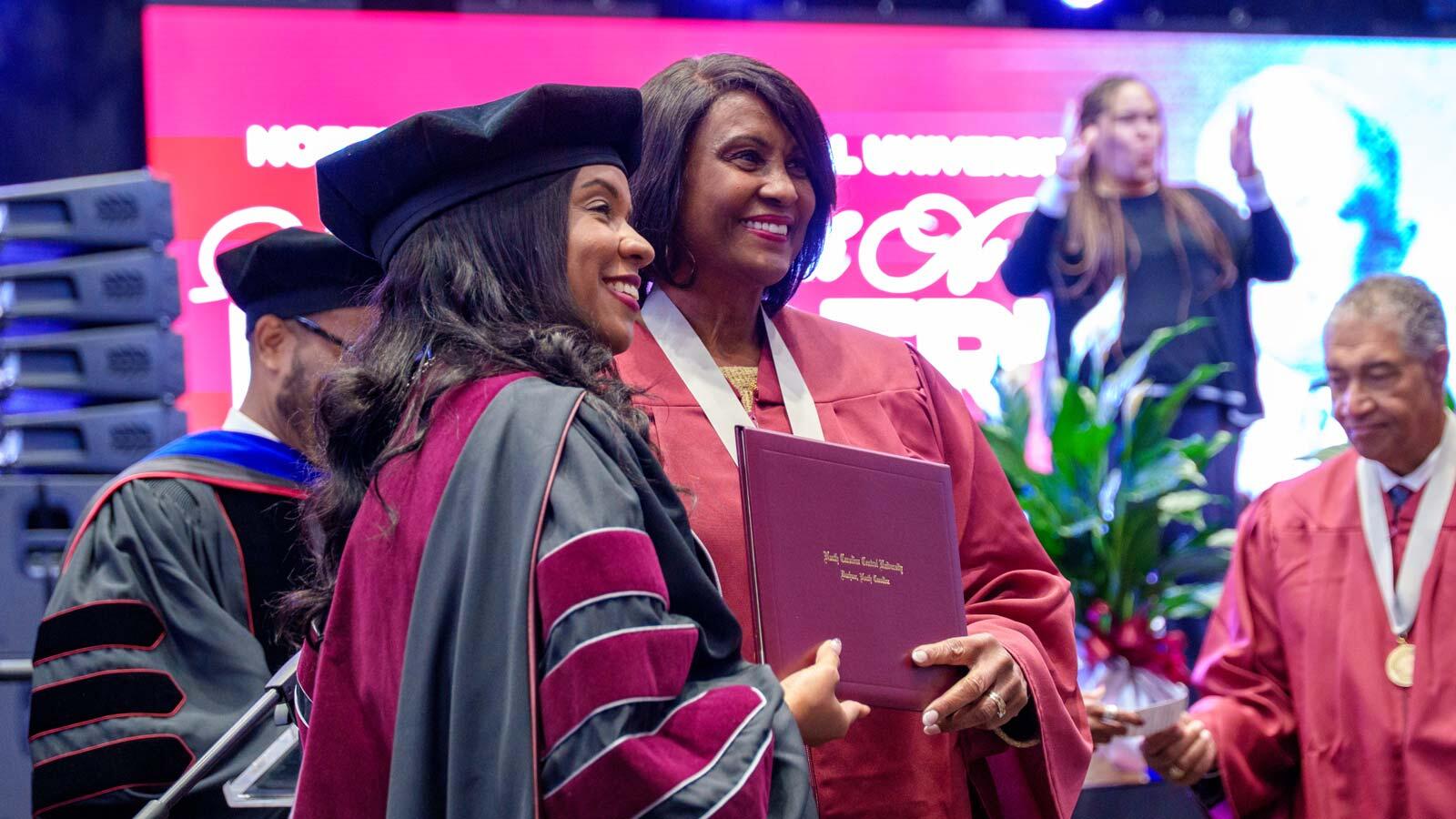 Chancellor Dixon smiles as she presents a diploma folder to a graduate at a North Carolina Central University commencement ceremony.