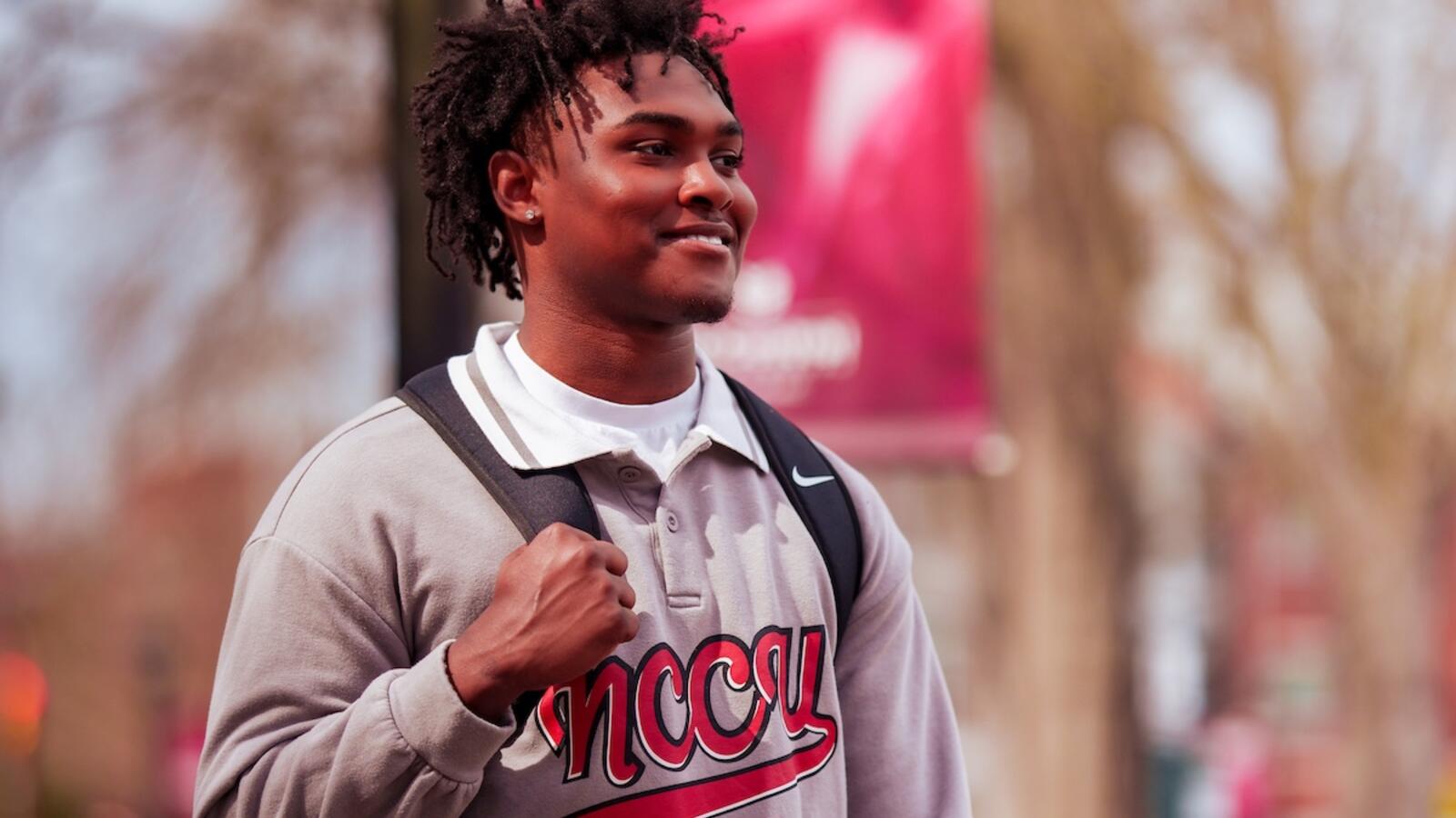 Student smiling and carrying a backpack and notebooks