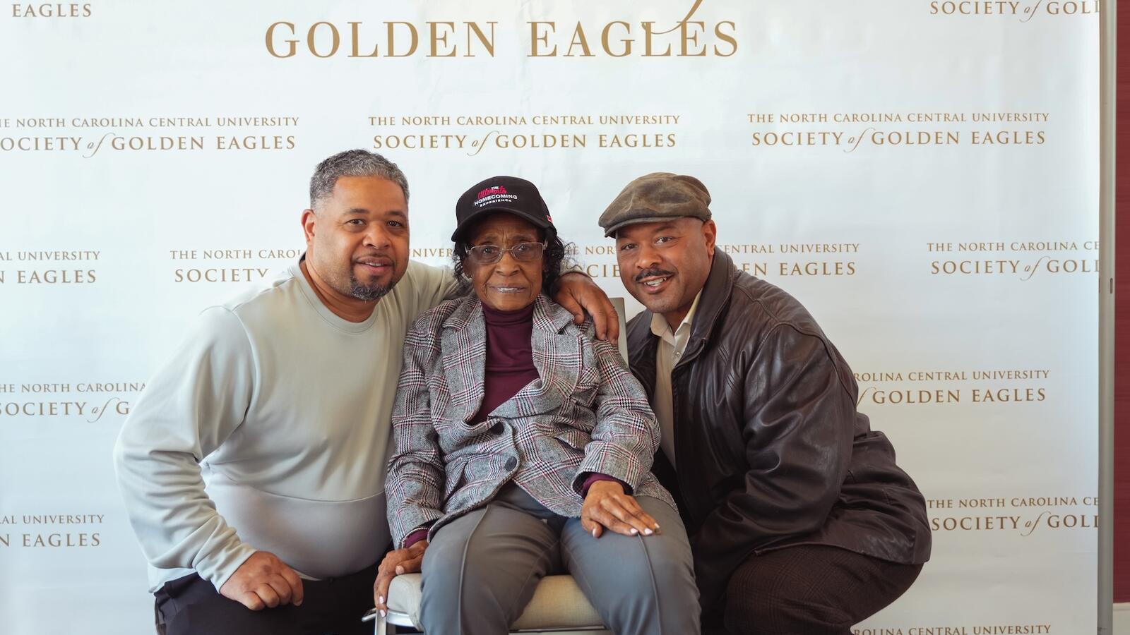 Three people pose in front of a backdrop that says "The Society of Golden Eagles"