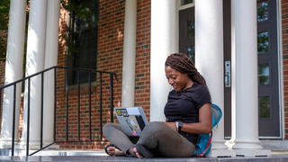Student sitting outside building working on laptop