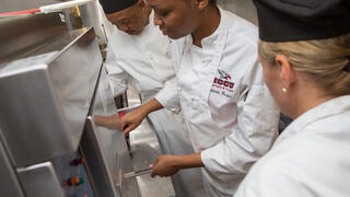 Three chefs oversee food cooking on stovetop.
