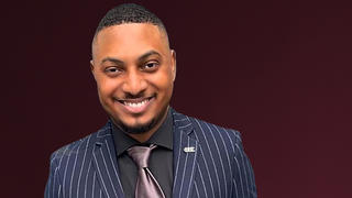 Man with black shirt and tie, smiling.