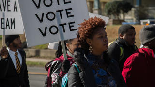 Marchers holding signs that say: Vote