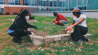 Workers weed the Campus Garden wearing gloves and facemasks.