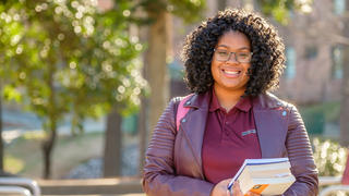 Woman with black curly hair holding textbooks.