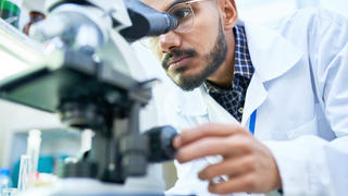 Man in white coat looking into microscope