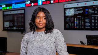 Student smiling in front of stock market screens
