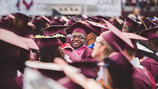 a student at commencement, smiling in a sea of graduates
