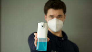 Man wearing a mask and holding out hand sanitizer.