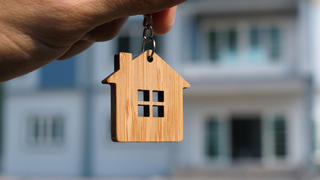 A person holding up a house keychain in front of a house
