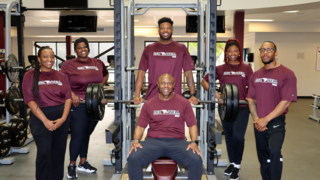 Members of the RecWell team standing and smiling around a bench press machine.