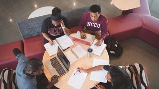 Four students sit at a small table studying together