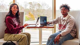 Two NCCU students sitting together with their laptops, smiling