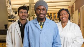 Three diverse lab members—two men and one woman—are smiling and posing in a science laboratory.