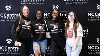 Four female students smiling in front of NCCU backdrop.