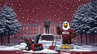 NCCU eagle mascot waving on snowy campus with snowblower and shovels near statue and academic building.