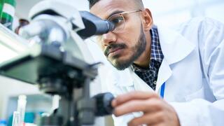 Research scientist in lab coat analyzing samples under microscope in university laboratory setting.