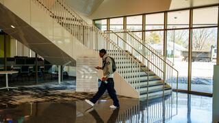 CCU student walks through a modern campus building lobby with large windows and staircase.