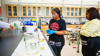 NCCU students in a science lab wearing safety goggles and gloves conducting hands-on experiments with lab equipment and materials.